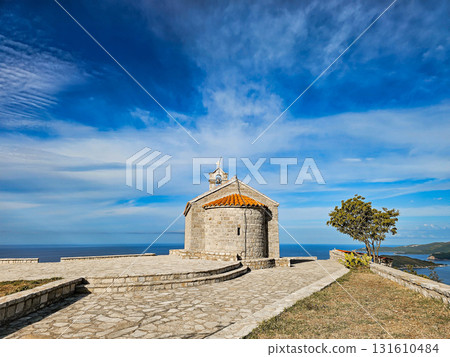 Scenic view of the Church of St. Sava on a hill near Sveti Stefan, Montenegro, with blue sky and clouds above. Traditional Montenegrin architecture and peaceful landscape. 131610484