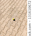 Yellow tennis ball on stone pavement. Single yellow tennis ball lying on patterned stone pavement under bright sunlight. Minimal outdoor background. 131610672
