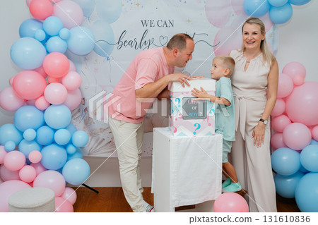 Father and son looking at decorated box, smiling mother nearby during baby shower celebration. Warm family moment for event promotion, parenting content and lifestyle imagery Father and son looking at decorated box, smiling mother nearby during baby shower celebration. Warm family moment for event promotion, parenting content and lifestyle imagery 131610836