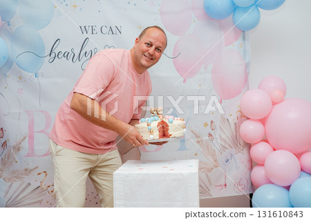 Smiling man with birthday cake at gender reveal celebration. Colorful balloons, family happiness and festive lifestyle editorial concept Smiling man with birthday cake at gender reveal celebration. Colorful balloons, family happiness and festive lifestyle editorial concept 131610843