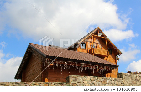 The roof and balcony of a wooden country house can be seen behind a stone fence The roof and balcony of a wooden country house can be seen behind a stone fence 131610905