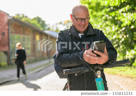 Portrait of a smiling senior man riding a electric kick scooter in city and using phone 131611231