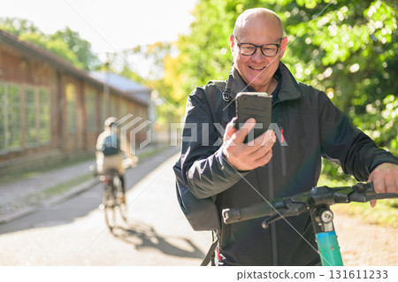 Portrait of a smiling senior man riding a electric kick scooter in city and using phone 131611233