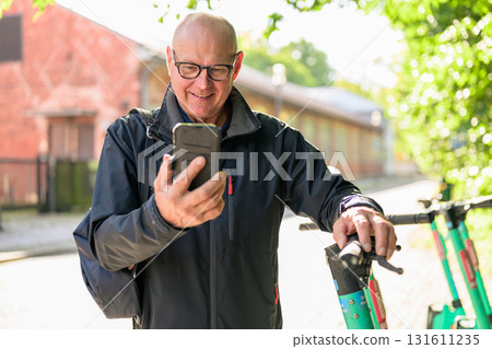 Portrait of a smiling senior man riding a electric kick scooter in city and using phone 131611235