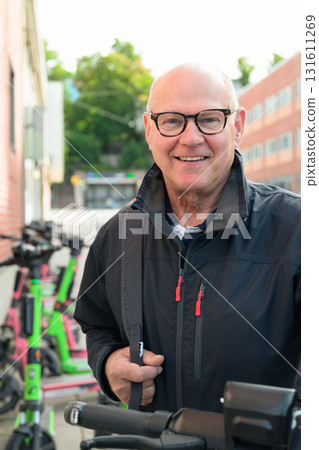 Portrait of a smiling bald senior man with an electric kick scooter in the city 131611269