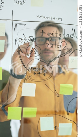 Business team collaborating on a project, using a glass board with sticky notes and marker to brainstorm ideas and develop a strategic plan in office space Business team collaborating on a project, using a glass board with sticky notes and marker to brainstorm ideas and develop a strategic plan in office space 131612385