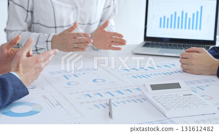 Business professionals discussing financial reports and data analysis during an office meeting, reviewing market trends and performance charts on paper and laptop Business professionals discussing financial reports and data analysis during an office meeting, reviewing market trends and performance charts on paper and laptop 131612482