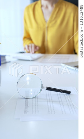 Magnifying glass placed near laptop on white desk, financial papers spread underneath, professional accounting workspace. Audit and taxes in business Magnifying glass placed near laptop on white desk, financial papers spread underneath, professional accounting workspace. Audit and taxes in business 131612489
