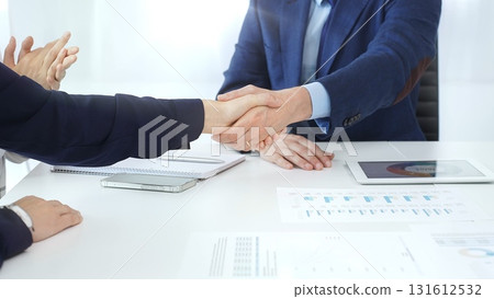 Business partners shaking hands at a meeting, celebrating successful negotiations and signing a contract, with documents, digital tablet, and smartphone on the table 131612532