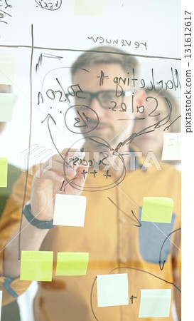 Business team collaborating on a project, using a glass board with sticky notes and marker to brainstorm ideas and develop a strategic plan in office space Business team collaborating on a project, using a glass board with sticky notes and marker to brainstorm ideas and develop a strategic plan in office space 131612617