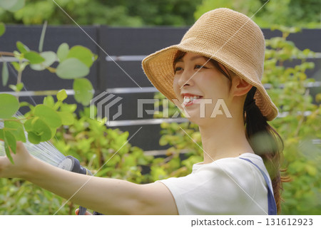 一位婦女正在花園裡小心翼翼地澆灌植物 一位婦女正在花園裡小心翼翼地澆灌植物 131612923