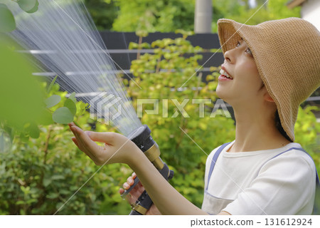 一位婦女正在花園裡小心翼翼地澆灌植物 一位婦女正在花園裡小心翼翼地澆灌植物 131612924