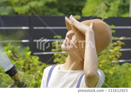 一位婦女正在花園裡小心翼翼地澆灌植物 一位婦女正在花園裡小心翼翼地澆灌植物 131612925