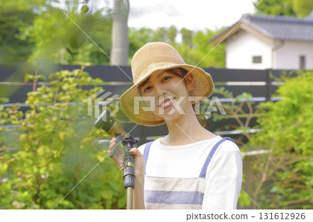 一位婦女正在花園裡小心翼翼地澆灌植物 一位婦女正在花園裡小心翼翼地澆灌植物 131612926