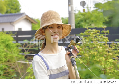一位婦女正在花園裡小心翼翼地澆灌植物 一位婦女正在花園裡小心翼翼地澆灌植物 131612927