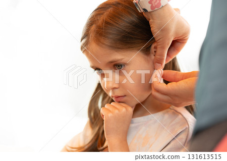 Mother putting earring on daughter ear in white Mother putting earring on daughter ear in white 131613515