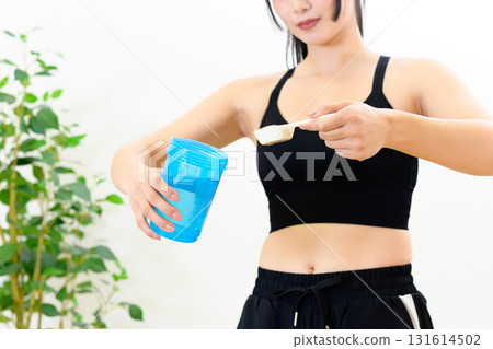 Woman putting protein powder into shaker, indoors, training wear, sports bra 131614502