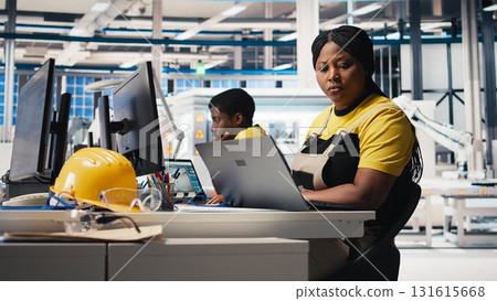 Black woman technician testing solar panel designs on industrial software, working in alternative energy manufacturing plant. Female engineer optimizing the production line. Camera B. 131615668