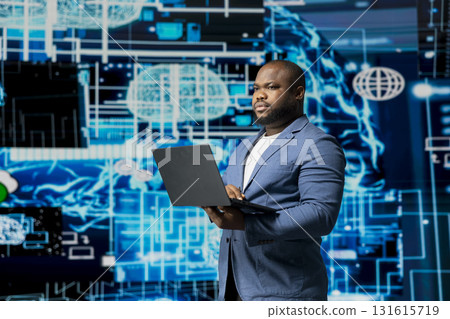 Black businessman using smart technology to interact with cybernetic platforms and AI interfaces, representing the integration of machine learning and predictive analytics in modern development. 131615719