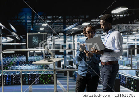 Programmers team in data center reviewing AI LLM visualizations on devices, monitoring hardware in server room. IT coworkers analyze neural network to ensure stable infrastructure operations. 131615793