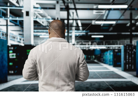 Engineer doing yearly checkup to prolong data center hardware life span and avoid downtime. African american employee in server room monitoring server infrastructure components Engineer doing yearly checkup to prolong data center hardware life span and avoid downtime. African american employee in server room monitoring server infrastructure components 131615863