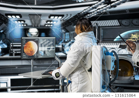 Astronaut in orbital station reviewing Mars planetary analytics on monitor. Spaceship crew member running telemetry software, doing Martian surface research to assist future planetary exploration 131615864