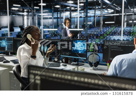 Admin in data center answers telephone call, assisting users with AI troubleshooting. Server farm IT specialist talks in phone call, managing clients issues using artificial intelligence 131615878