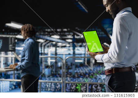 African american technician using copy space display on tablet, solving software development tasks on industrial platform. Young man visualizing infrastructure engineering in server room. African american technician using copy space display on tablet, solving software development tasks on industrial platform. Young man visualizing infrastructure engineering in server room. 131615903