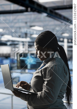 Female engineer in data center using laptop to configure hardware specifically optimized for AI tasks. Woman doing maintenance on rigs performing load balancing for artificial intelligence computing 131615907