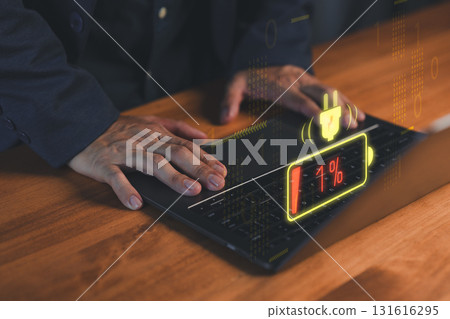 Close-up of hands on a laptop computer with a glowing low-battery warning icon at 1%. Concept of technology failure, digital burnout, device charging issues, energy crisis and urgent solutions. 131616295