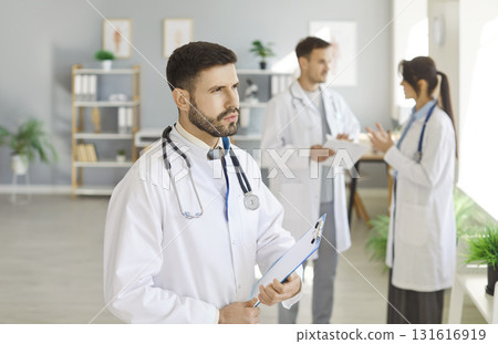 Serious and focused male medic coworker thinking, clinic team collaboration, leader with colleagues  131616919