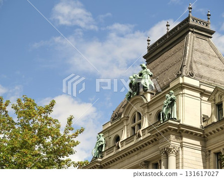 Historic building with sculptures under clear blue sky and fluffy clouds in city park Historic building with sculptures under clear blue sky and fluffy clouds in city park 131617027
