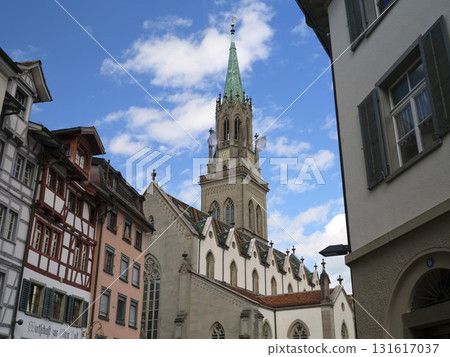 Historic church tower stands tall among colorful buildings in a serene town setting with a clear blue sky 131617037