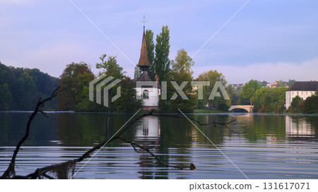 Scenic view of a quaint church surrounded by water and lush trees at sunset in a peaceful landscape Scenic view of a quaint church surrounded by water and lush trees at sunset in a peaceful landscape 131617071