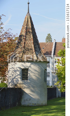 Historic tower with a pointed roof in a scenic garden setting during a sunny day 131617114