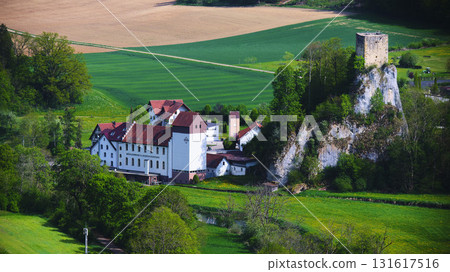 Historic castle overlooks rural landscape with lush fields and quaint buildings during a sunny day in the countryside 131617516