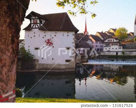 Charming riverside view of historic building reflecting in tranquil waters during early evening light Charming riverside view of historic building reflecting in tranquil waters during early evening light 131617528