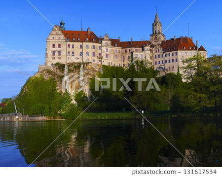 Historic castle perched on rocky cliff with reflection in calm water at sunset 131617534
