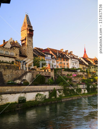 Beautiful riverside view of historical buildings and a tower during sunset in a charming town Beautiful riverside view of historical buildings and a tower during sunset in a charming town 131617536