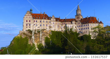 Beautiful historic castle perched on a hill surrounded by lush greenery under a clear blue sky 131617537