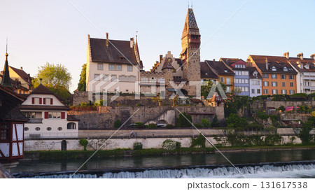 Historic buildings overlook a serene river during golden hour in a picturesque town near the water Historic buildings overlook a serene river during golden hour in a picturesque town near the water 131617538
