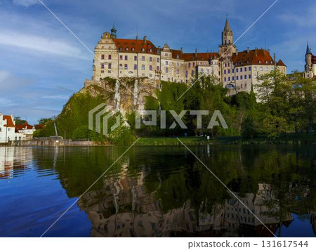Historic castle reflects beautifully on calm water during bright sunny day in picturesque landscape 131617544