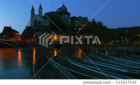 Nighttime view of a historic town with illuminated buildings and boats by the river in Switzerland 131617545