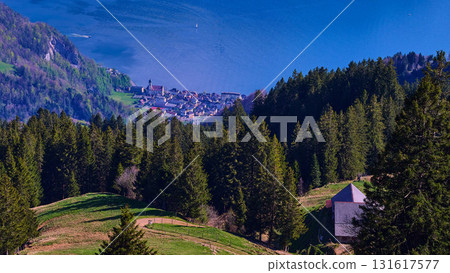 Scenic view of a lakeside town surrounded by mountains and forests in Switzerland under bright blue sky Scenic view of a lakeside town surrounded by mountains and forests in Switzerland under bright blue sky 131617577