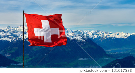 Swiss flag waves proudly against a backdrop of snow-capped mountains and clear blue skies in the Swiss Alps during daytime 131617588