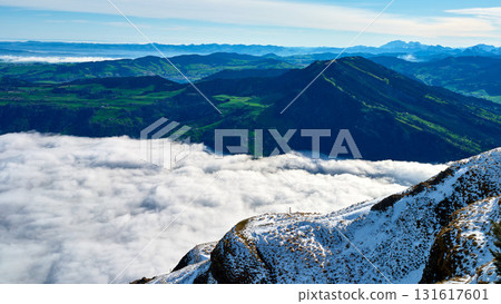 Mountain landscape with snow and clouds during bright daylight near lush green valleys in a serene environment 131617601