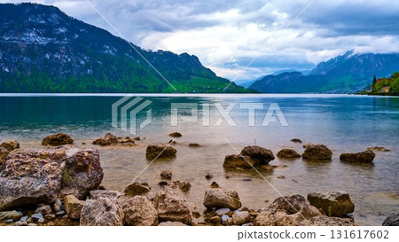 Scenic lakeside view featuring rocky shoreline with mountains and cloudy sky in Switzerland during springtime 131617602