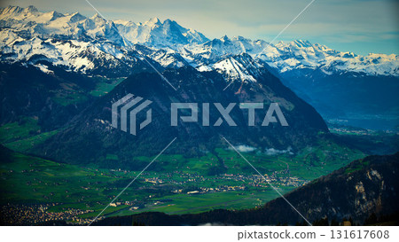 Snow-capped mountains offer stunning views over green valleys and small villages in Switzerland on a clear day 131617608