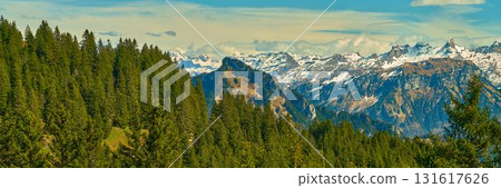 Mountains rise majestically above lush green forests in a picturesque alpine landscape during early afternoon light Mountains rise majestically above lush green forests in a picturesque alpine landscape during early afternoon light 131617626