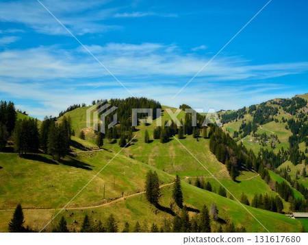 Lush green hills under a bright blue sky with scattered clouds during daytime 131617680